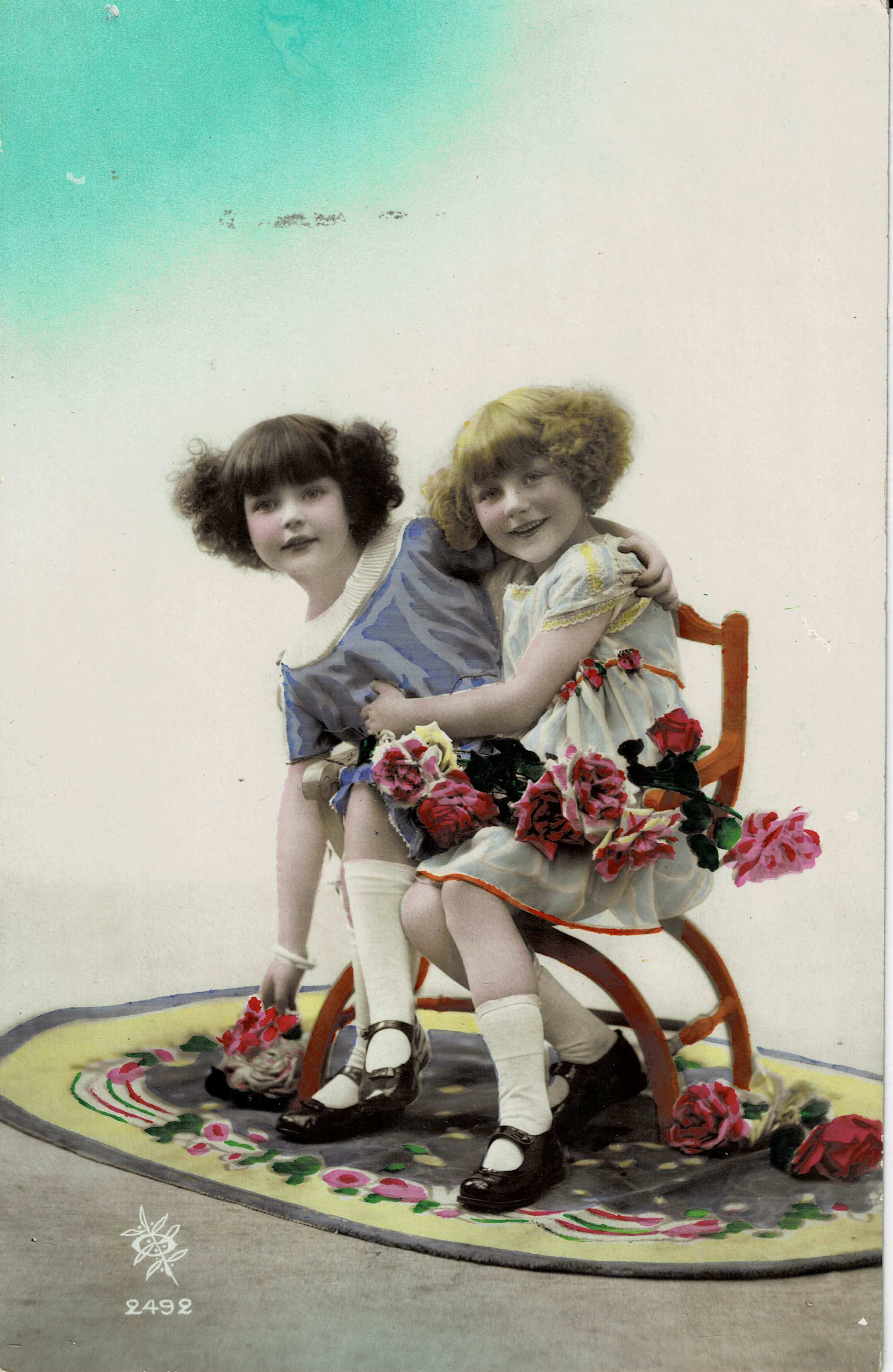 POSTAL NIÑAS SENTADAS EN UNA SILLA CON FLORES.